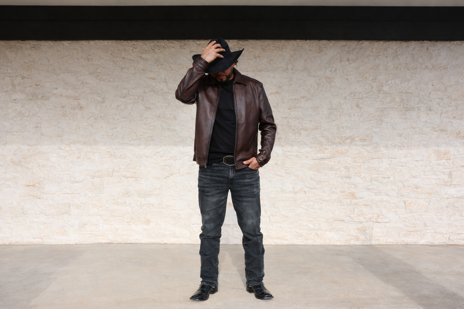 Person wearing a brown leather jacket and black hat against a light-colored wall.